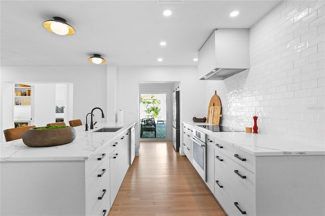 kitchen with stainless steel appliances, white cabinetry, sink, and wall chimney exhaust hood