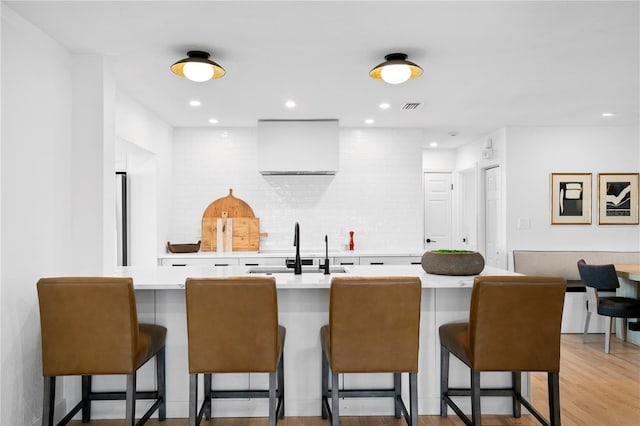 kitchen featuring sink, tasteful backsplash, white cabinetry, a kitchen breakfast bar, and light hardwood / wood-style floors