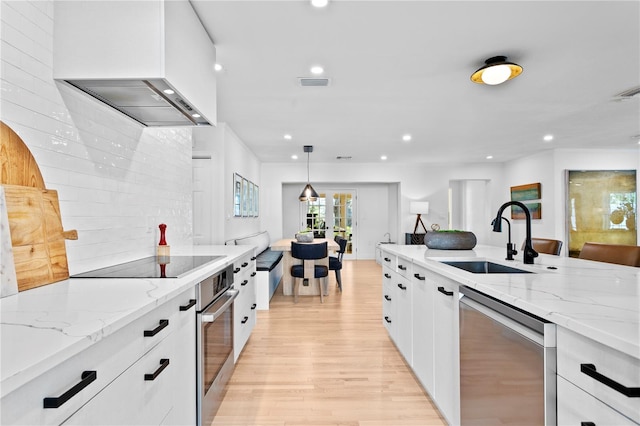 kitchen with white cabinetry, sink, stainless steel appliances, light stone countertops, and wall chimney range hood