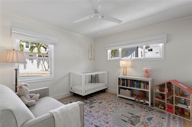 bedroom with hardwood / wood-style floors, crown molding, a crib, and ceiling fan