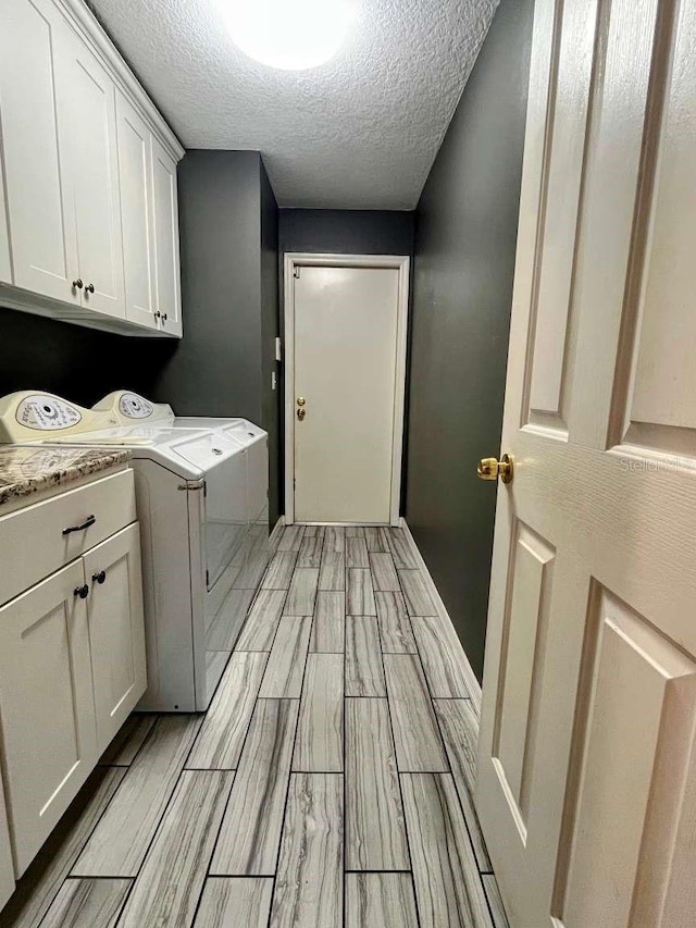 clothes washing area with cabinets, washer and dryer, and a textured ceiling