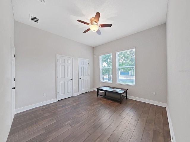 unfurnished bedroom with ceiling fan, dark hardwood / wood-style flooring, and two closets