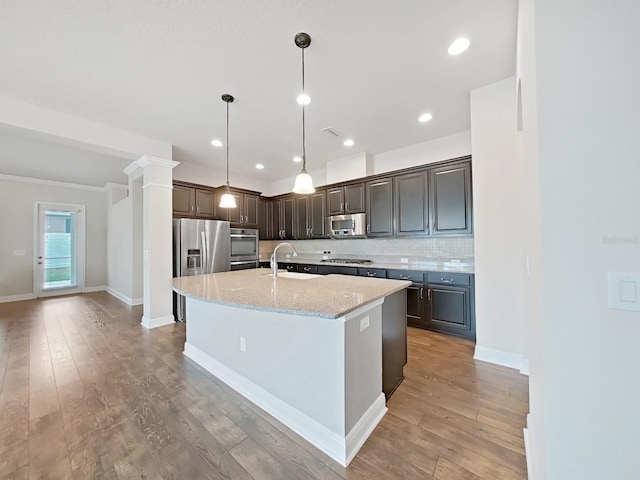 kitchen with decorative backsplash, appliances with stainless steel finishes, light stone countertops, sink, and a center island with sink