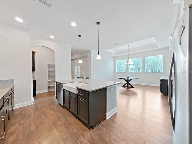 kitchen featuring sink, a raised ceiling, pendant lighting, a center island with sink, and appliances with stainless steel finishes