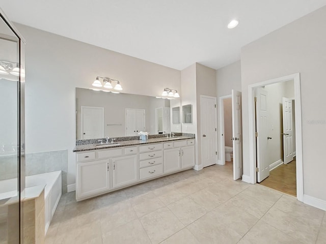 bathroom with tile patterned flooring, vanity, a relaxing tiled tub, and toilet