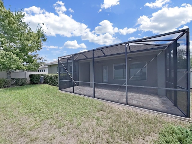 back of property with a yard, glass enclosure, and a patio area