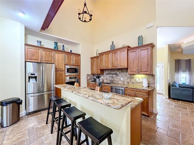 kitchen featuring appliances with stainless steel finishes, a towering ceiling, backsplash, a kitchen bar, and beam ceiling