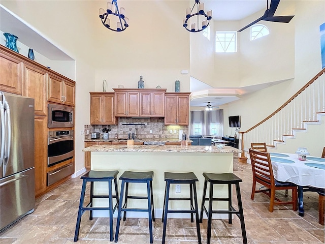 kitchen featuring appliances with stainless steel finishes, a towering ceiling, a kitchen island, tasteful backsplash, and light stone countertops