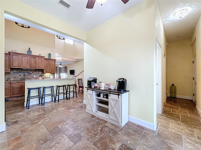 kitchen with backsplash, a kitchen breakfast bar, a high ceiling, ceiling fan, and kitchen peninsula