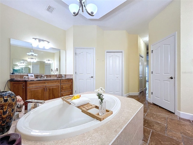 bathroom featuring vanity, a relaxing tiled tub, and an inviting chandelier