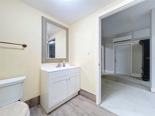 bathroom featuring vanity, a textured ceiling, a wall unit AC, and toilet