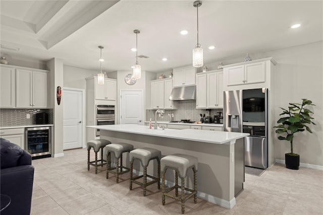 kitchen with white cabinetry, hanging light fixtures, wine cooler, a kitchen island with sink, and appliances with stainless steel finishes