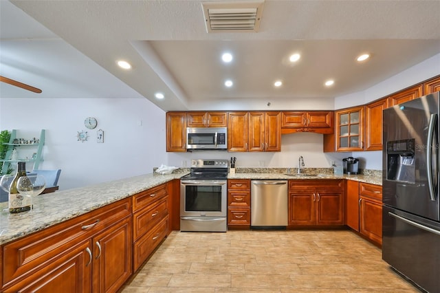 kitchen featuring appliances with stainless steel finishes, kitchen peninsula, light stone counters, and sink