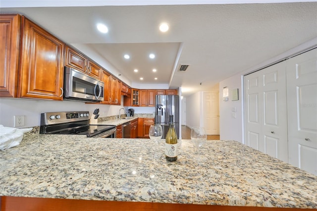 kitchen featuring appliances with stainless steel finishes, sink, light stone countertops, and kitchen peninsula