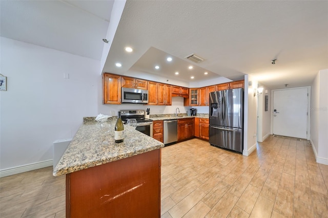 kitchen with light stone counters, kitchen peninsula, light hardwood / wood-style flooring, stainless steel appliances, and sink