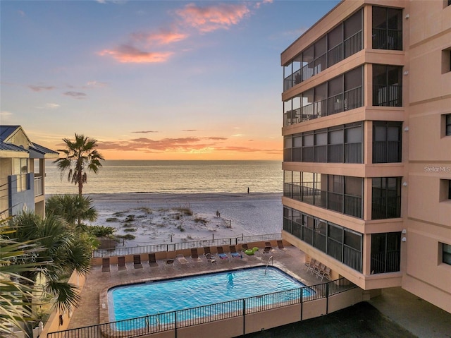 pool at dusk featuring a beach view and a water view