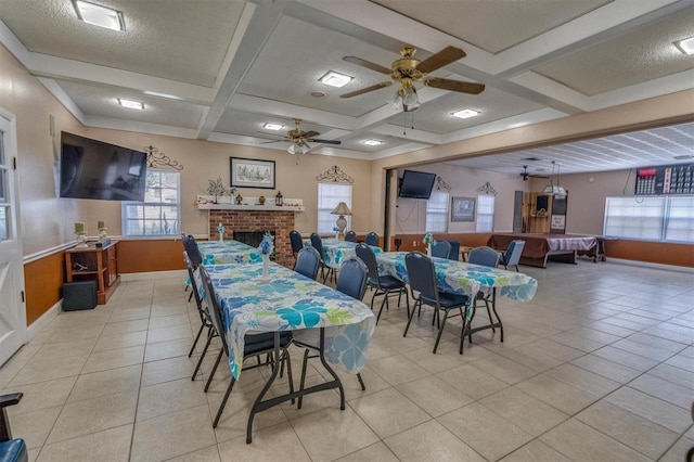 tiled dining space with beamed ceiling, ceiling fan, a fireplace, and coffered ceiling