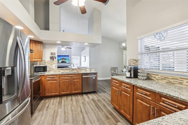 kitchen with light stone counters, stainless steel appliances, a towering ceiling, backsplash, and sink