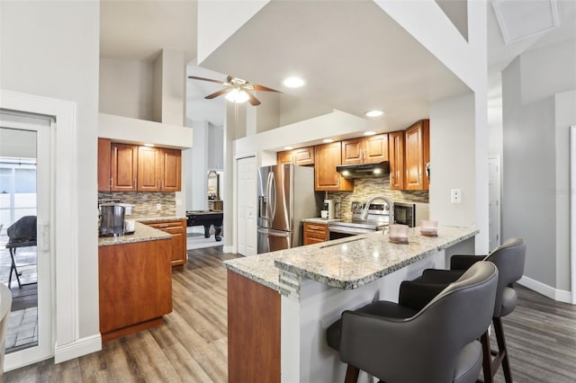 kitchen with light stone counters, kitchen peninsula, a breakfast bar area, a high ceiling, and appliances with stainless steel finishes