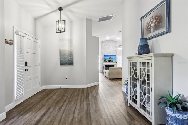 entrance foyer featuring lofted ceiling, dark hardwood / wood-style flooring, an inviting chandelier, and a stone fireplace