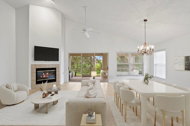 living room with a textured ceiling, a tiled fireplace, light tile patterned flooring, ceiling fan with notable chandelier, and a high ceiling