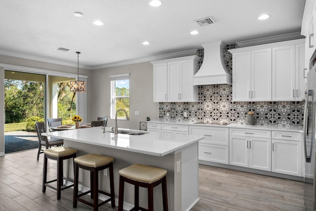 kitchen with sink, light hardwood / wood-style flooring, premium range hood, white cabinetry, and an island with sink