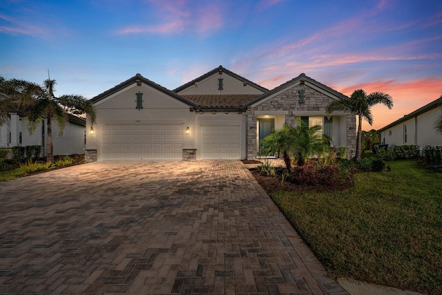 ranch-style house with decorative driveway, stucco siding, a garage, stone siding, and a tiled roof