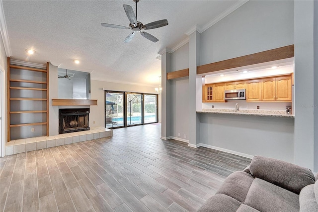 unfurnished living room featuring a tiled fireplace, a textured ceiling, ceiling fan, and crown molding