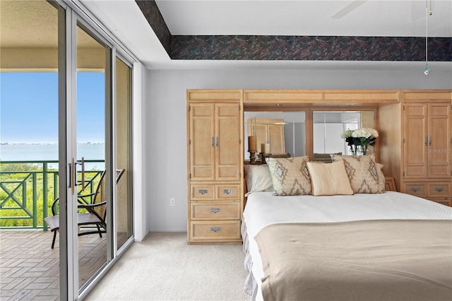 bedroom with ceiling fan, light colored carpet, access to exterior, and a water view