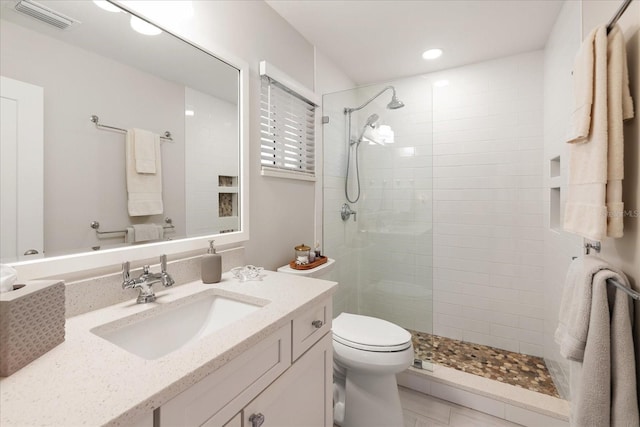 bathroom featuring tile patterned floors, toilet, vanity, and a tile shower