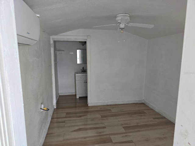 unfurnished room featuring ceiling fan, light wood-type flooring, lofted ceiling, and a wall unit AC