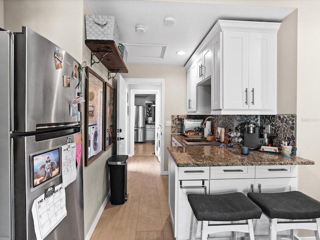 kitchen featuring dark stone countertops, sink, stainless steel refrigerator, and white cabinets