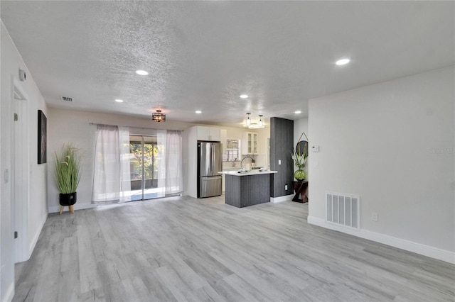 unfurnished living room featuring sink, a chandelier, a textured ceiling, and light hardwood / wood-style flooring