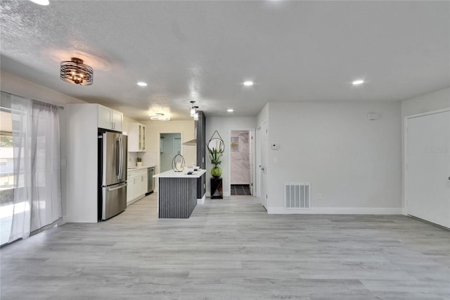 kitchen featuring white cabinetry, a textured ceiling, light wood-type flooring, stainless steel appliances, and a kitchen island with sink