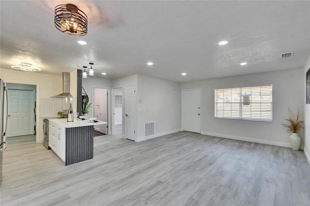 kitchen with white cabinets, stainless steel range with electric cooktop, light hardwood / wood-style floors, a textured ceiling, and wall chimney exhaust hood