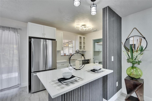 kitchen featuring stainless steel refrigerator, white cabinetry, backsplash, light hardwood / wood-style floors, and decorative light fixtures