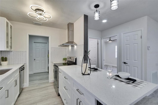 kitchen featuring wall chimney range hood, stainless steel appliances, tasteful backsplash, light stone counters, and white cabinets