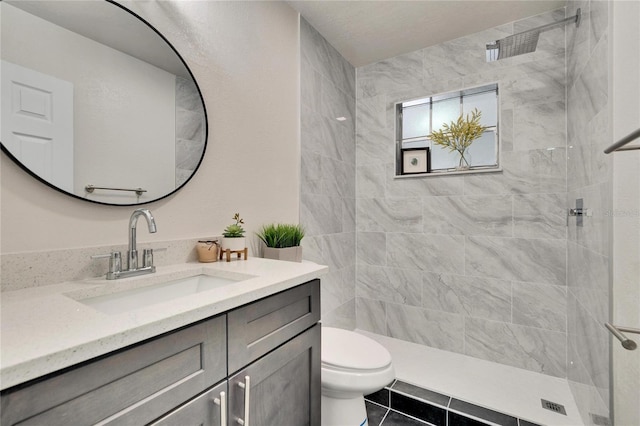 bathroom featuring vanity, tile patterned floors, toilet, and a tile shower