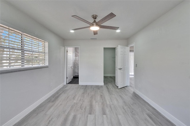 unfurnished bedroom with light hardwood / wood-style flooring, ceiling fan, connected bathroom, a walk in closet, and a closet