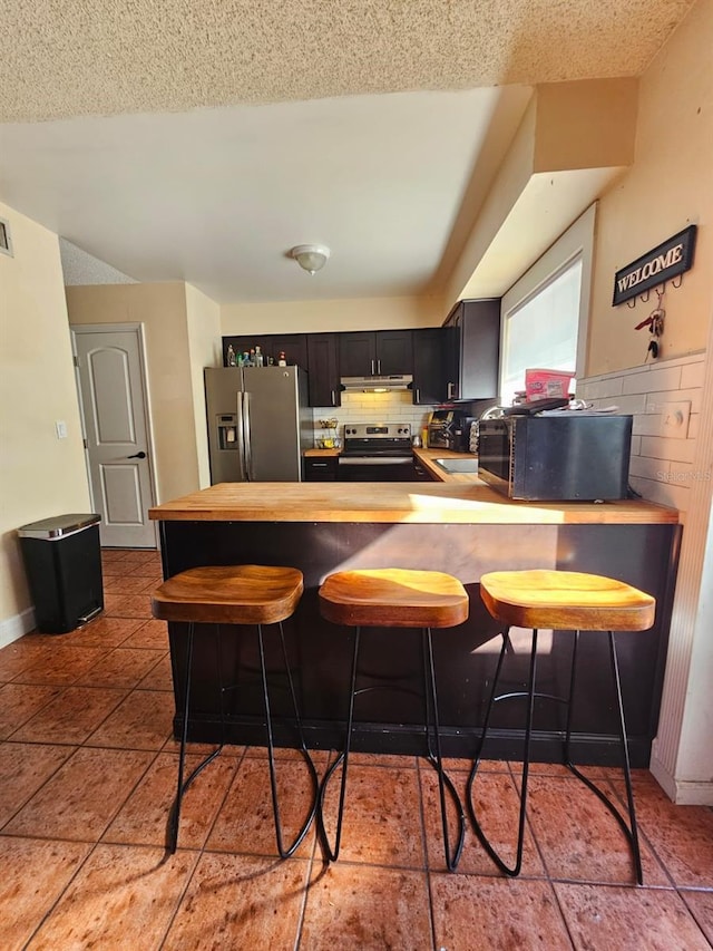 kitchen with tile patterned floors, kitchen peninsula, a breakfast bar, and appliances with stainless steel finishes