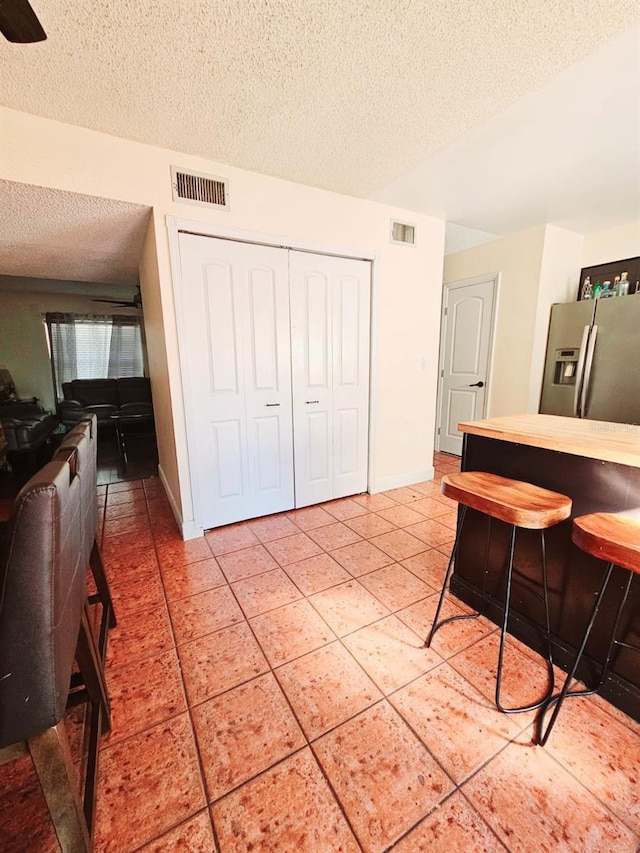 interior space with a kitchen breakfast bar, tile patterned flooring, a textured ceiling, and stainless steel refrigerator with ice dispenser