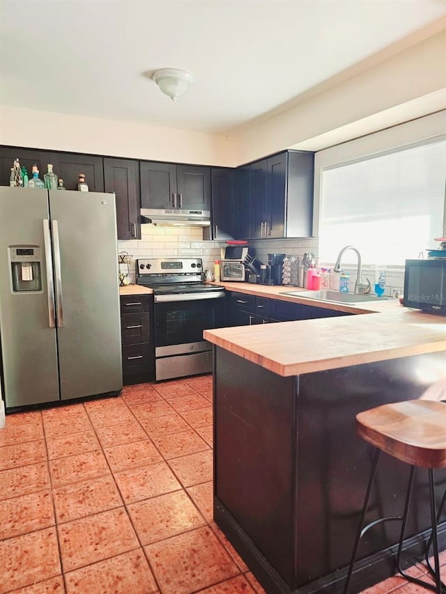 kitchen with a breakfast bar, sink, light tile patterned floors, kitchen peninsula, and stainless steel appliances