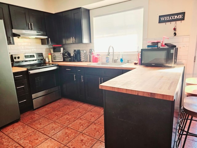 kitchen featuring sink, stainless steel appliances, wood counters, decorative backsplash, and light tile patterned flooring