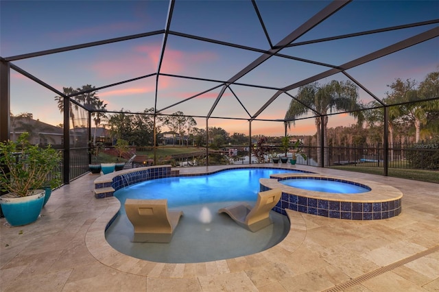 pool at dusk with a lanai, a patio area, and an in ground hot tub