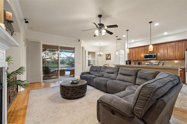 living room with crown molding, ceiling fan with notable chandelier, and light wood-type flooring