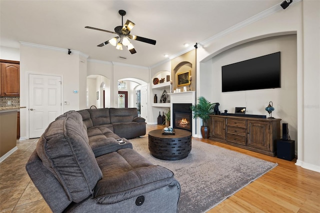 living room featuring built in shelves, ceiling fan, ornamental molding, and light hardwood / wood-style floors