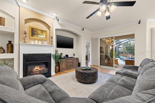 living room with crown molding, ceiling fan, light hardwood / wood-style floors, and built in features