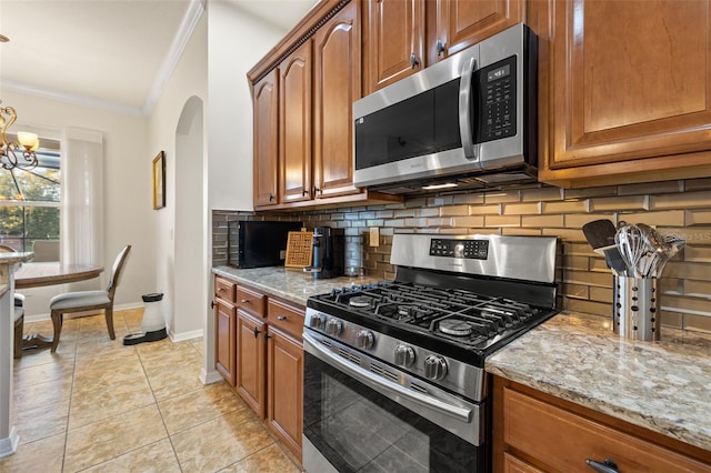 kitchen with light stone counters, crown molding, a chandelier, light tile patterned floors, and stainless steel appliances