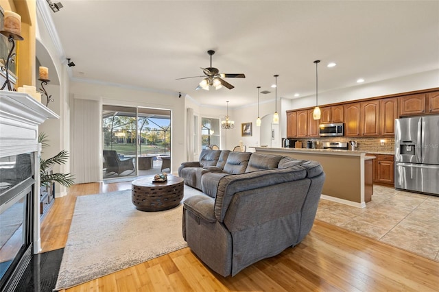 living room featuring ornamental molding, ceiling fan with notable chandelier, a high end fireplace, and light hardwood / wood-style floors