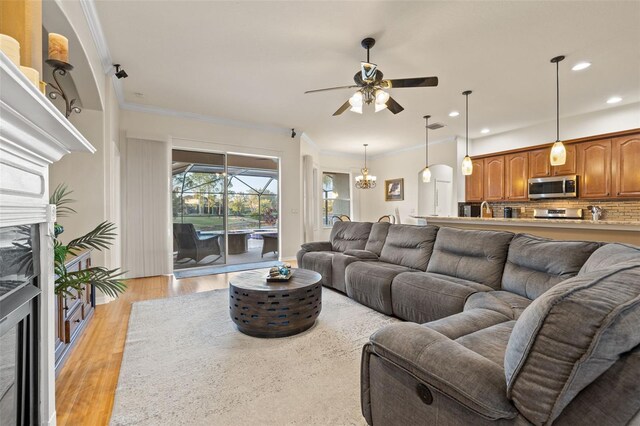 living room featuring crown molding, a premium fireplace, ceiling fan with notable chandelier, and light hardwood / wood-style floors